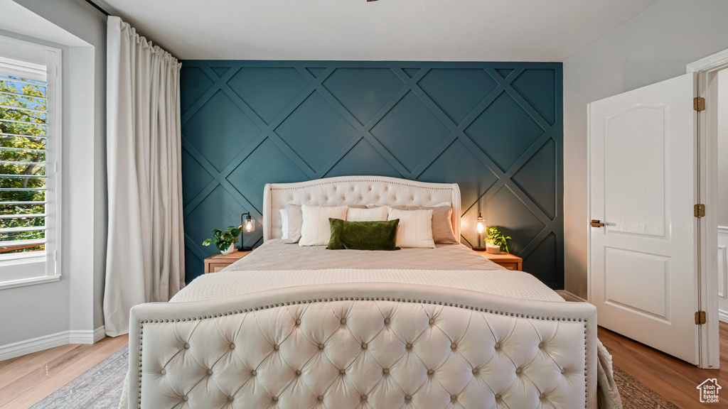 Bedroom with a decorative wall, baseboards, and light wood finished floors