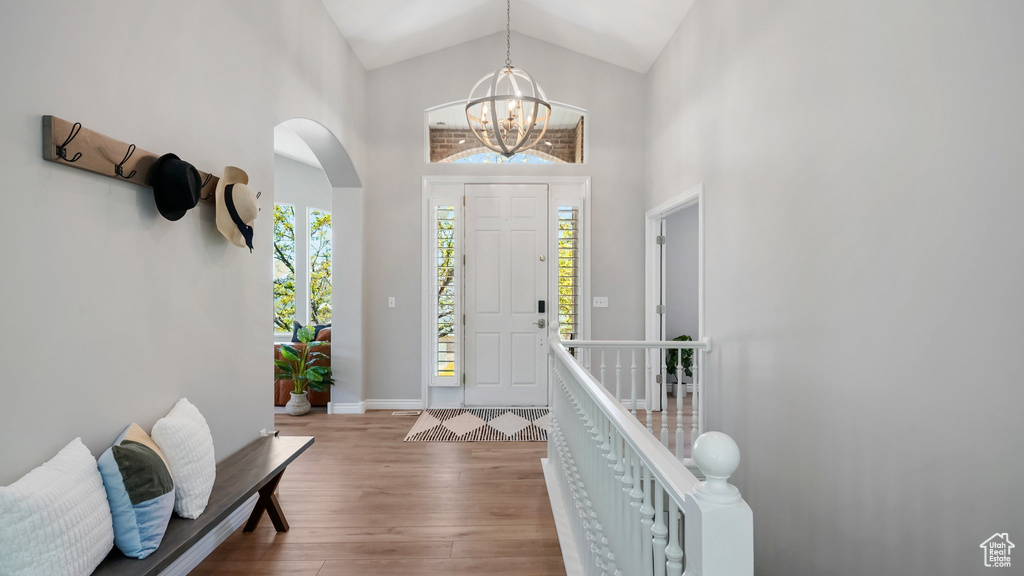 Entryway featuring wood finished floors, arched walkways, a chandelier, high vaulted ceiling, and baseboards