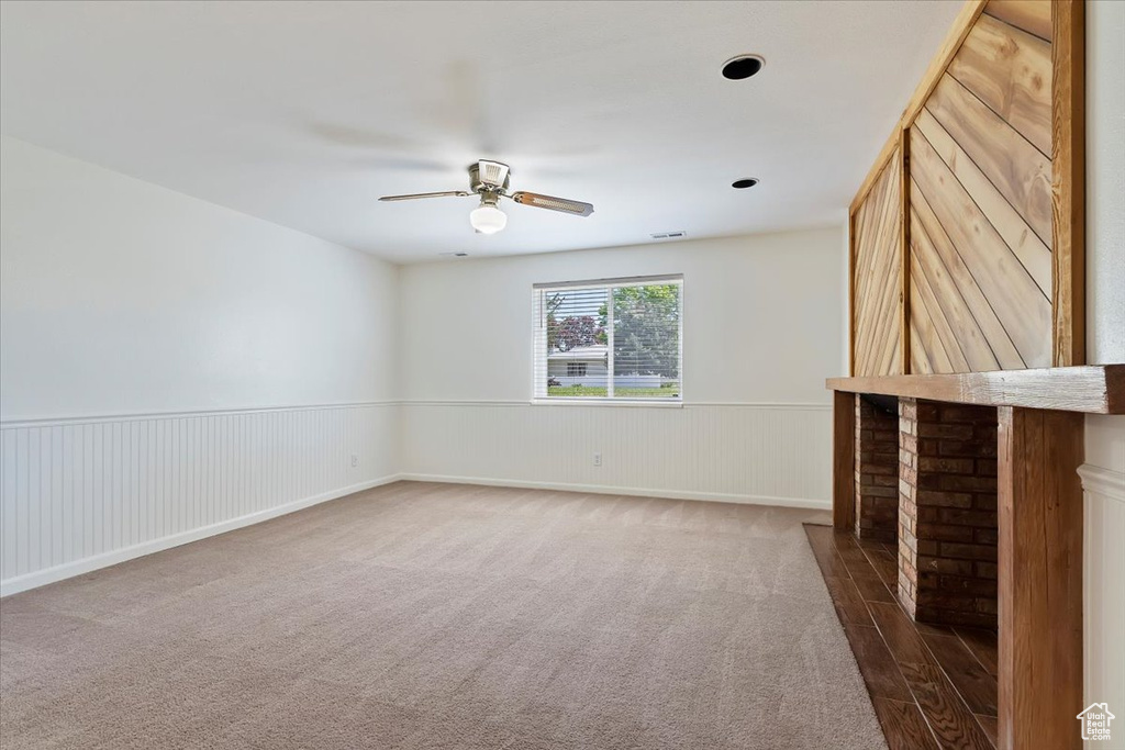 Carpeted empty room featuring a ceiling fan and a wainscoted wall