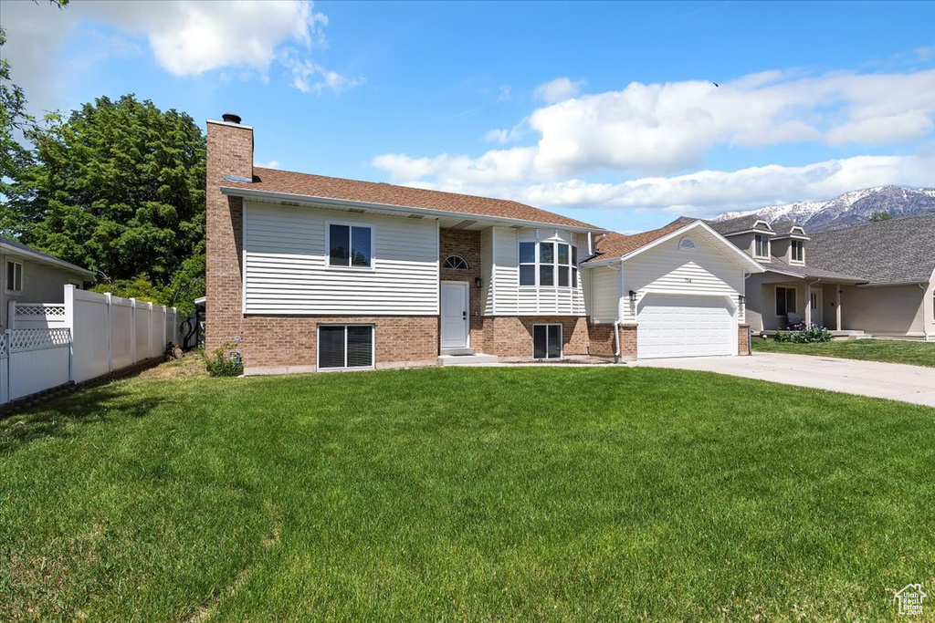 Split foyer home featuring brick siding, an attached garage, driveway, and a chimney