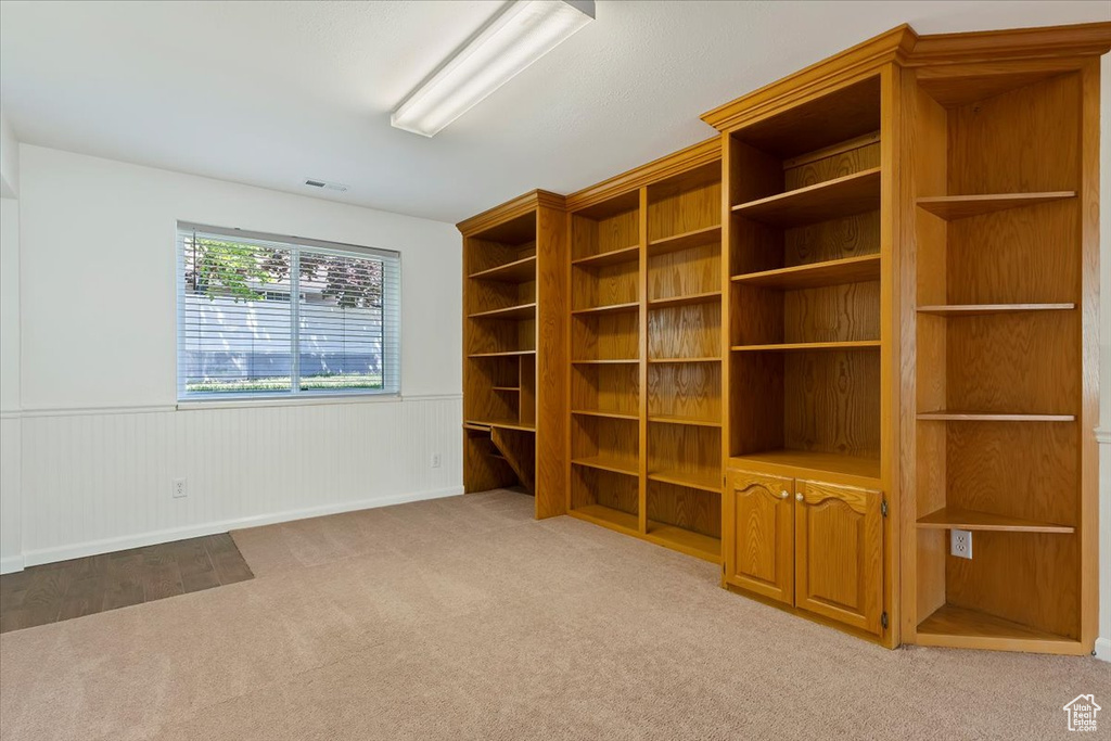 Empty room featuring light colored carpet, a wainscoted wall, and baseboards