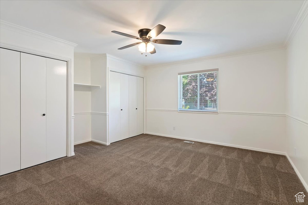 Unfurnished bedroom featuring carpet floors, two closets, ornamental molding, baseboards, and ceiling fan