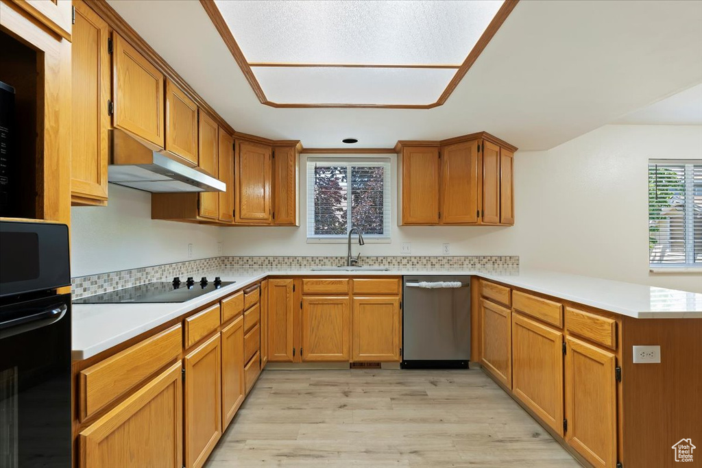 Kitchen with black appliances, a sink, a peninsula, under cabinet range hood, and light wood-type flooring
