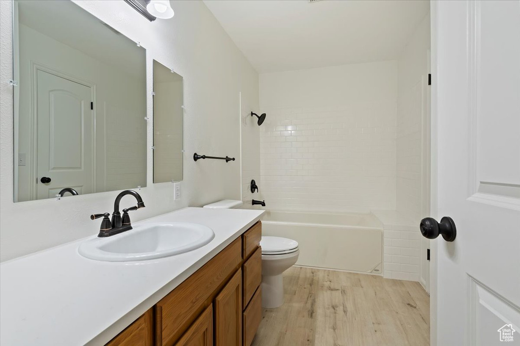 Bathroom with wood finished floors, toilet, vanity, and  shower combination