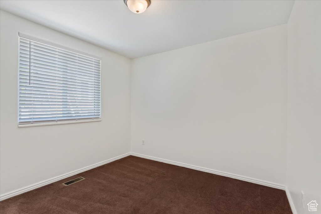 Spare room featuring dark carpet and baseboards