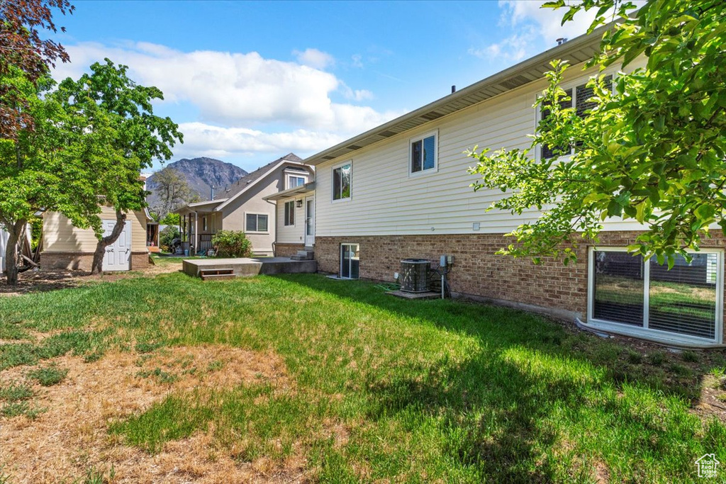 Back of property with a yard, brick siding, a mountain view, and central AC unit