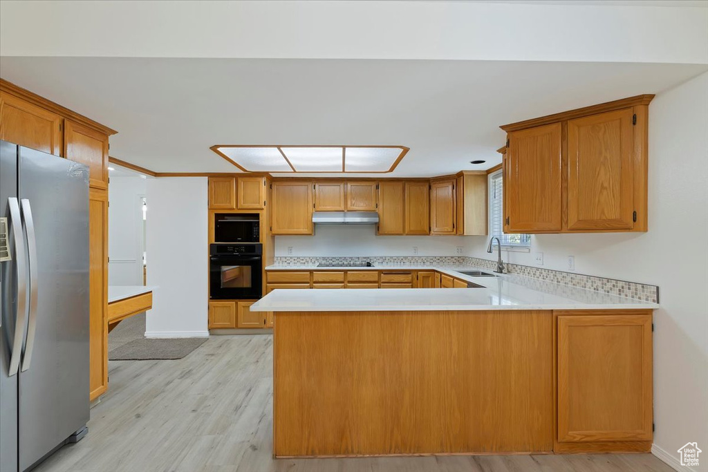 Kitchen featuring black appliances, under cabinet range hood, a sink, a peninsula, and light countertops