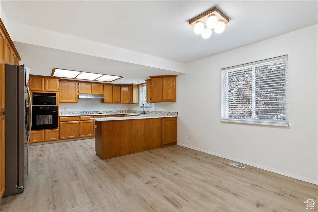 Kitchen with black appliances, a peninsula, light wood-style floors, and baseboards
