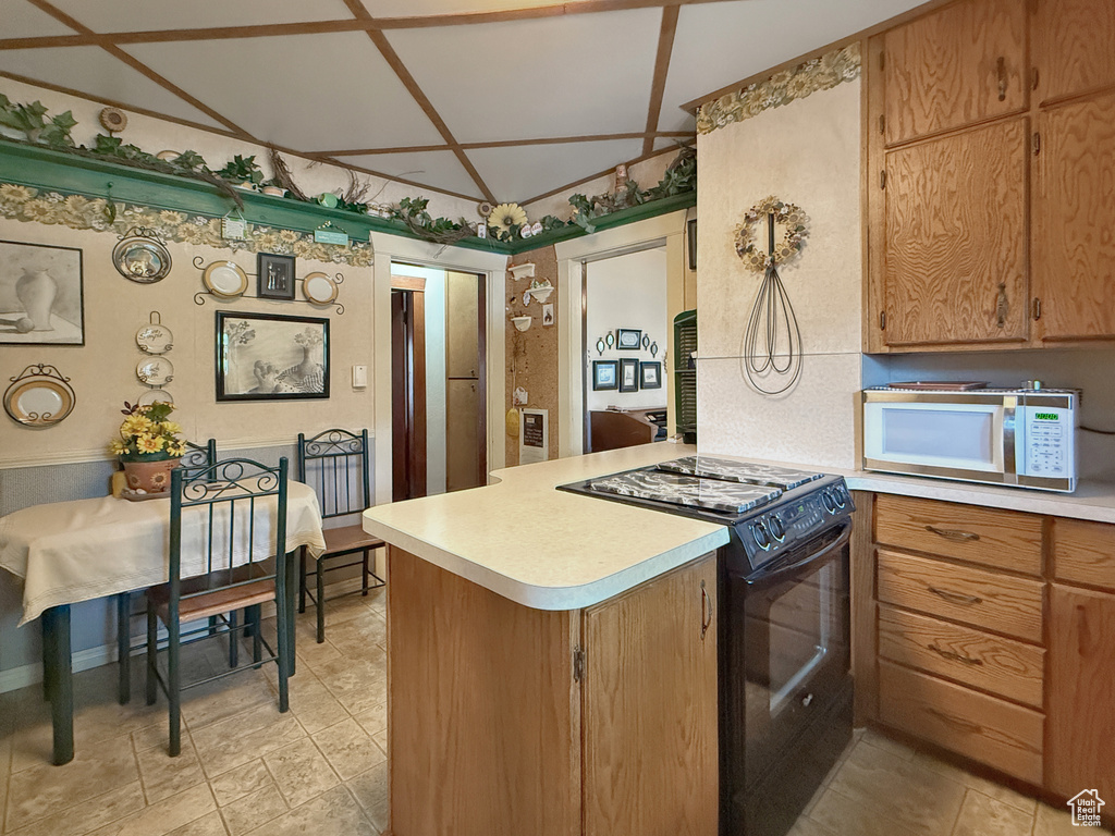 Kitchen featuring black range with electric stovetop, white microwave, light countertops, and a peninsula
