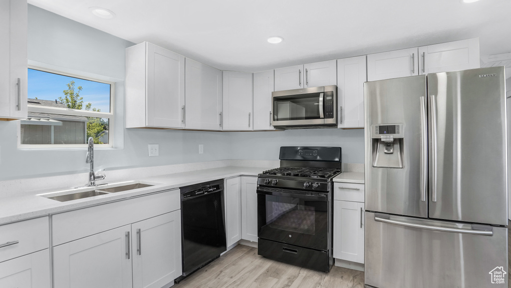 Kitchen with black appliances, a sink, white cabinetry, light countertops, and light wood-style flooring