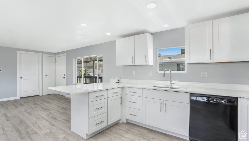 Kitchen with black dishwasher, a sink, a peninsula, light wood-style floors, and light countertops