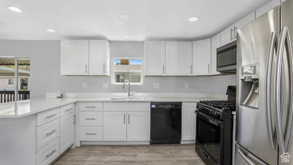 Kitchen with black appliances, a sink, a peninsula, light countertops, and white cabinetry