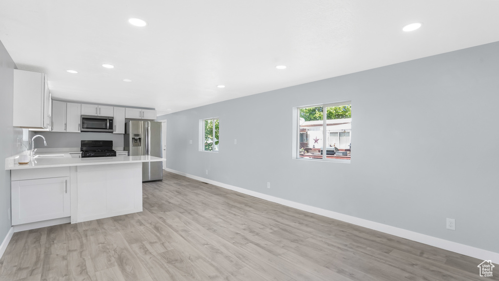 Kitchen with appliances with stainless steel finishes, light countertops, a sink, a peninsula, and baseboards