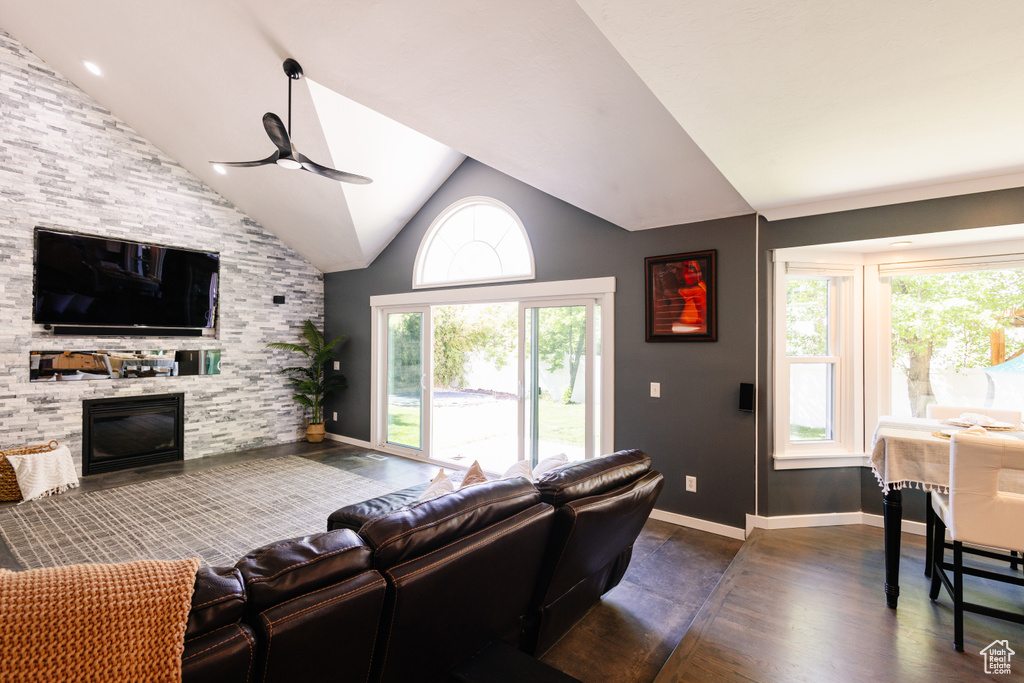 Living area with a ceiling fan, dark wood finished floors, a stone fireplace, baseboards, and high vaulted ceiling