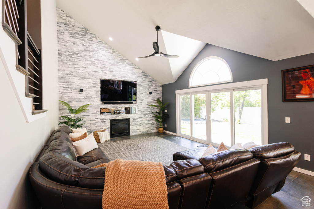 Living area with a ceiling fan, a stone fireplace, high vaulted ceiling, and baseboards