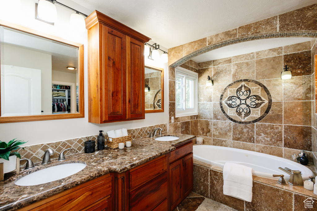 Full bath with tiled bath, double vanity, tile walls, a walk in closet, and backsplash