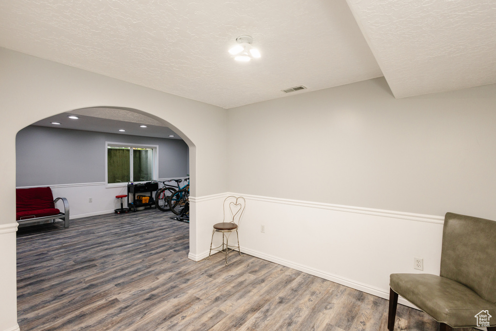 Living area with wood finished floors, arched walkways, a textured ceiling, baseboards, and recessed lighting