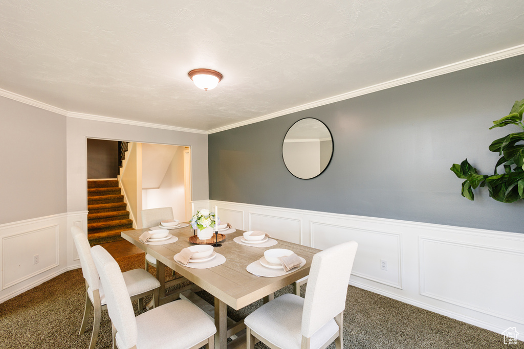 Dining area featuring carpet floors, wainscoting, ornamental molding, a decorative wall, and stairway