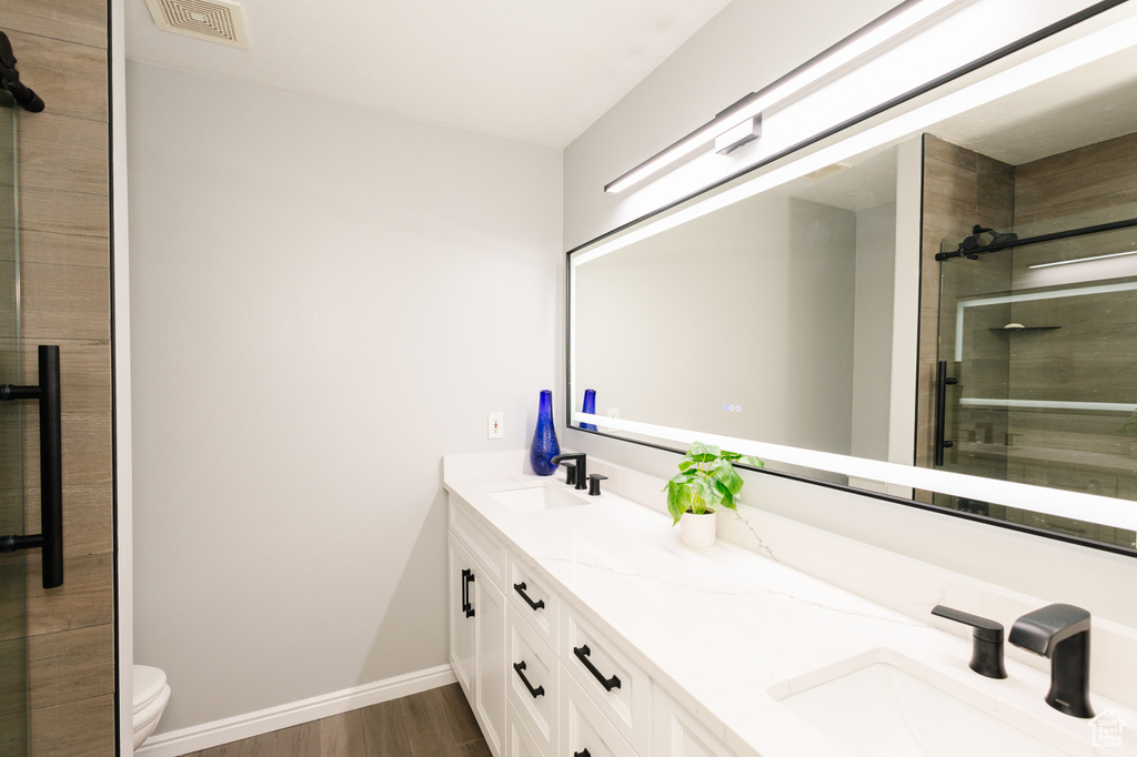 Bathroom featuring a shower stall, wood finished floors, double vanity, baseboards, and toilet