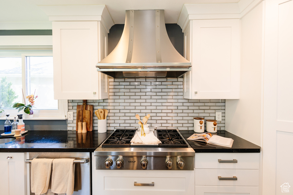 Kitchen with island exhaust hood, stainless steel gas stovetop, dark countertops, backsplash, and white cabinets