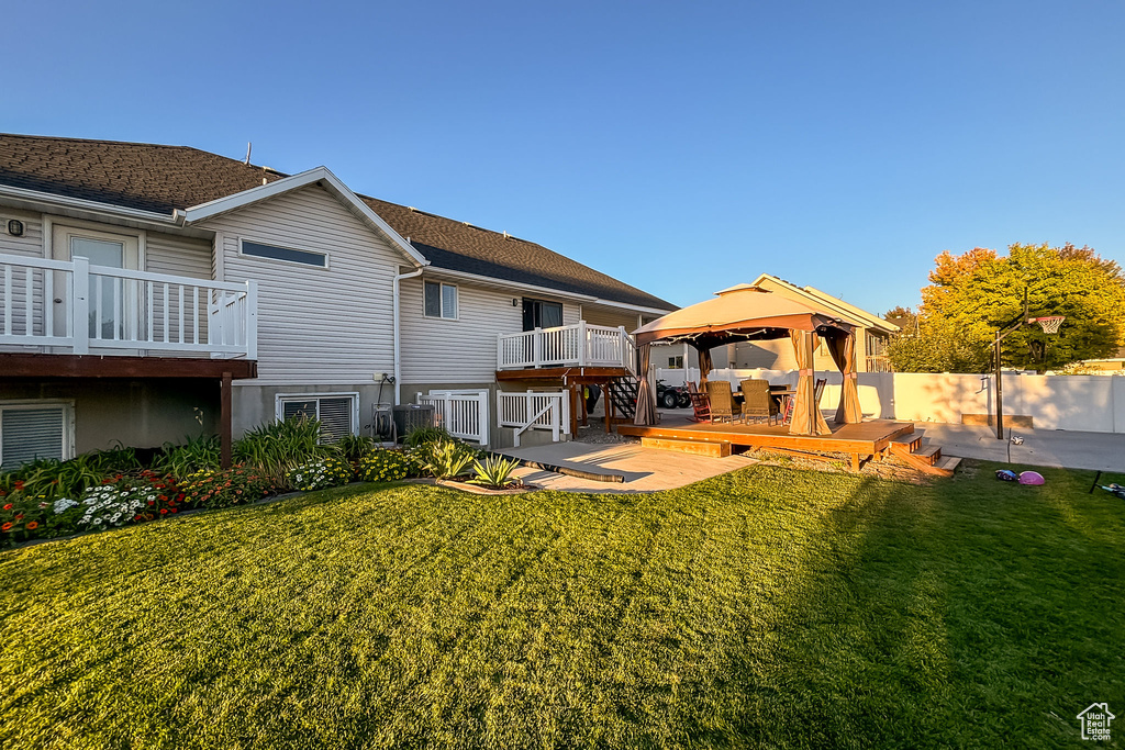 Back of property with a gazebo, a yard, a wooden deck, and a shingled roof