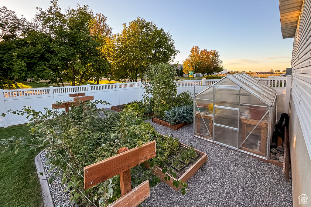 Fenced backyard featuring a greenhouse, a garden, and an outdoor structure