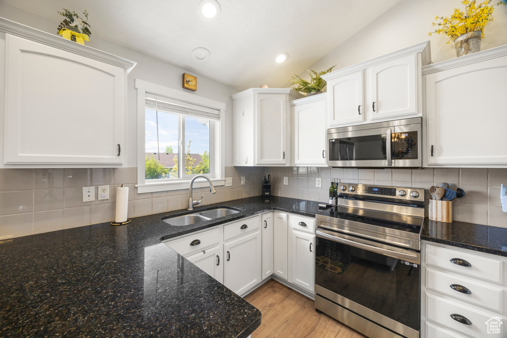 Kitchen with appliances with stainless steel finishes, a sink, vaulted ceiling, white cabinets, and backsplash