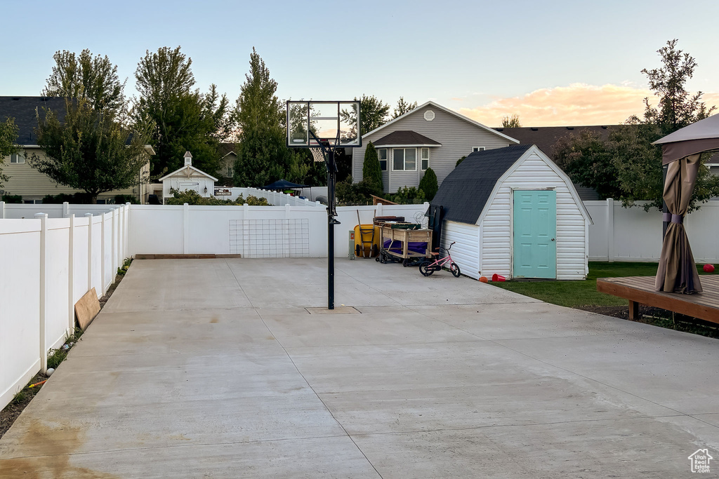 Patio terrace at dusk featuring a storage shed, a fenced backyard, and an outbuilding