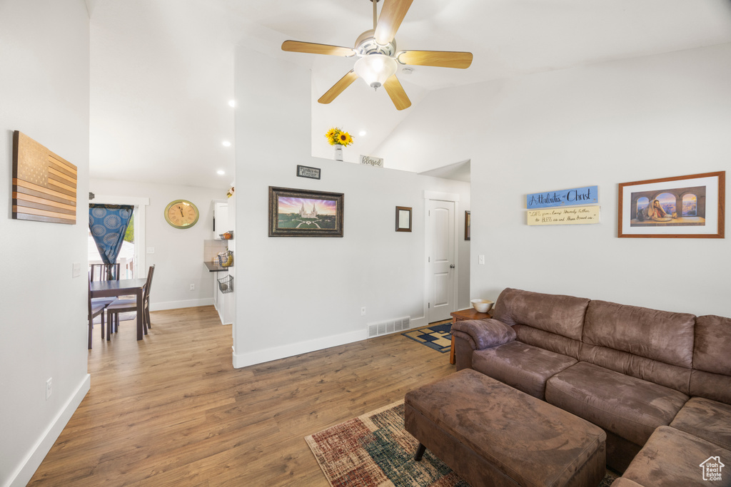 Living room with high vaulted ceiling, ceiling fan, light wood-style flooring, baseboards, and recessed lighting