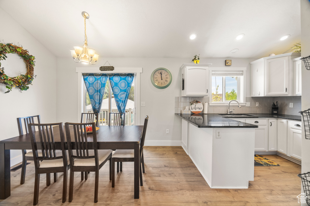 Kitchen with dark countertops, a chandelier, a sink, white cabinets, and tasteful backsplash