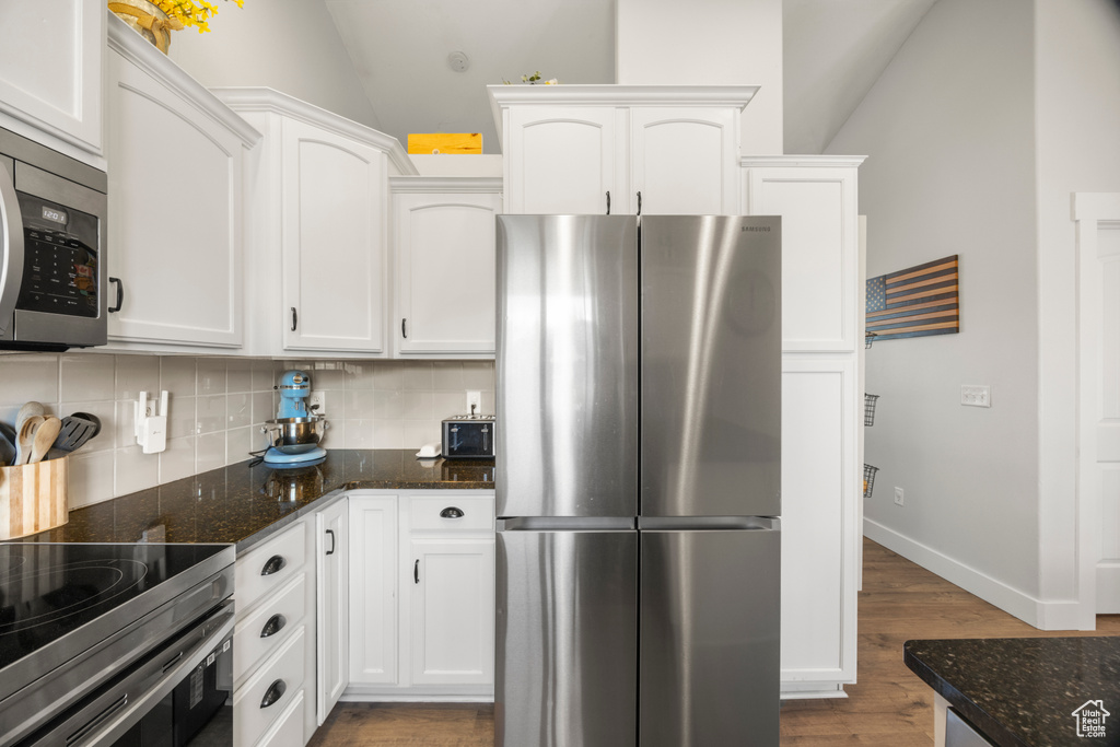 Kitchen with appliances with stainless steel finishes, tasteful backsplash, wood finished floors, white cabinets, and lofted ceiling