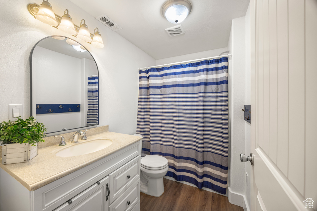 Bathroom featuring toilet, vanity, wood finished floors, and a shower with shower curtain