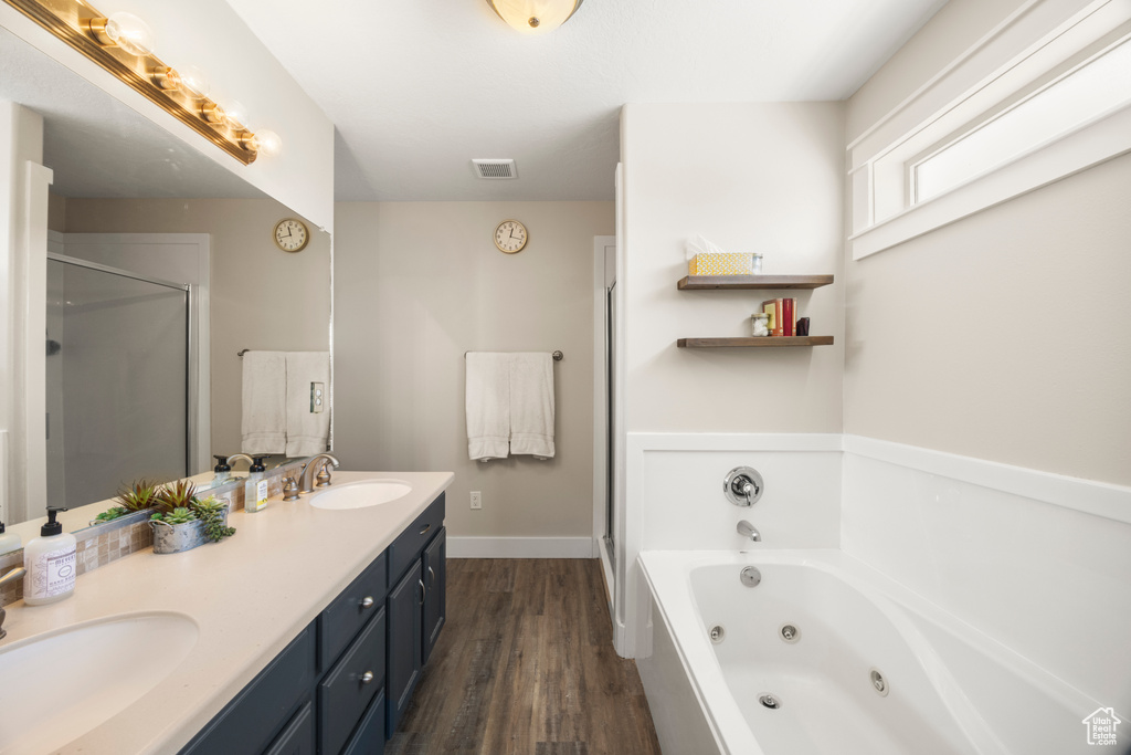 Full bathroom with wood finished floors, a tub with jets, a shower stall, double vanity, and baseboards