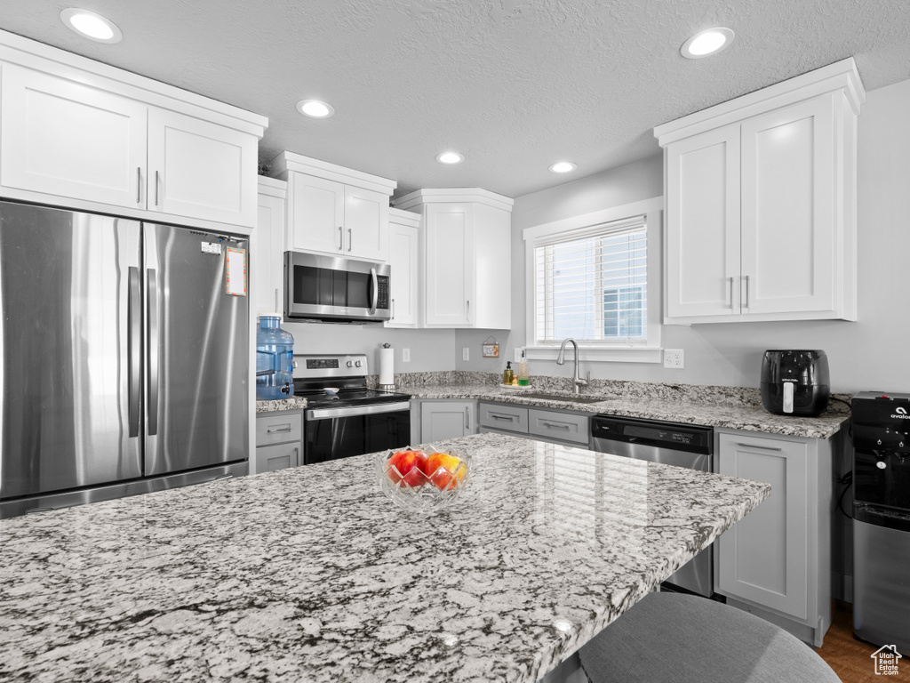 Kitchen featuring appliances with stainless steel finishes, a sink, recessed lighting, light stone counters, and white cabinetry