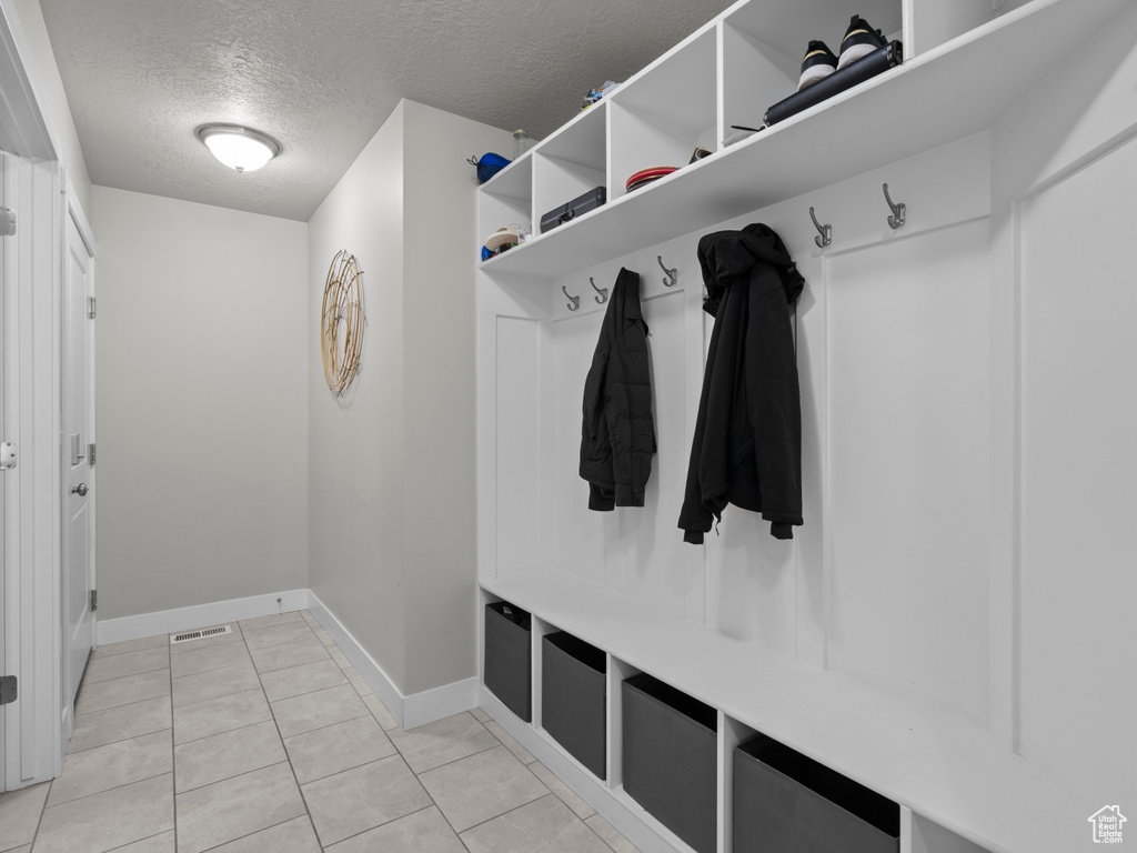 Mudroom featuring a textured ceiling, baseboards, and light tile patterned floors