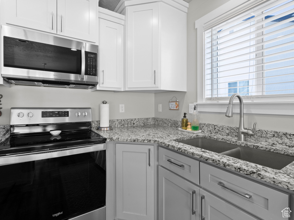 Kitchen with appliances with stainless steel finishes, a sink, white cabinets, and light stone counters