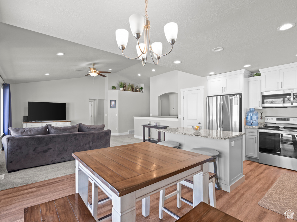 Dining area featuring lofted ceiling, ceiling fan, recessed lighting, light wood-style flooring, and a chandelier