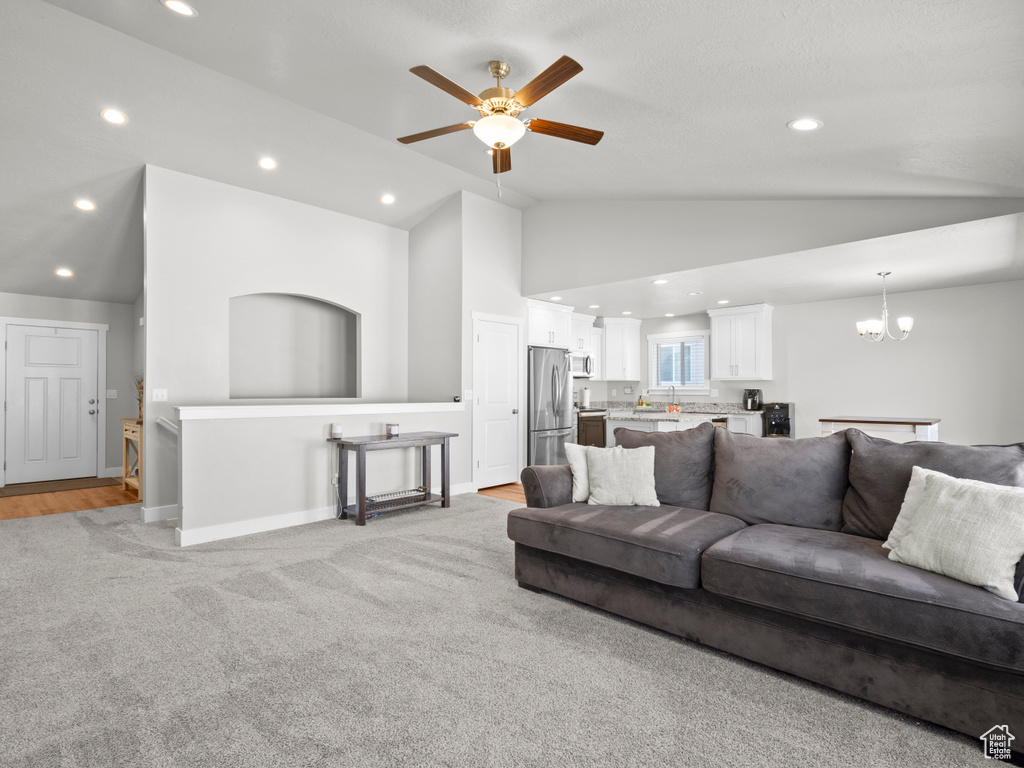 Living room with lofted ceiling, recessed lighting, a ceiling fan, a chandelier, and light colored carpet