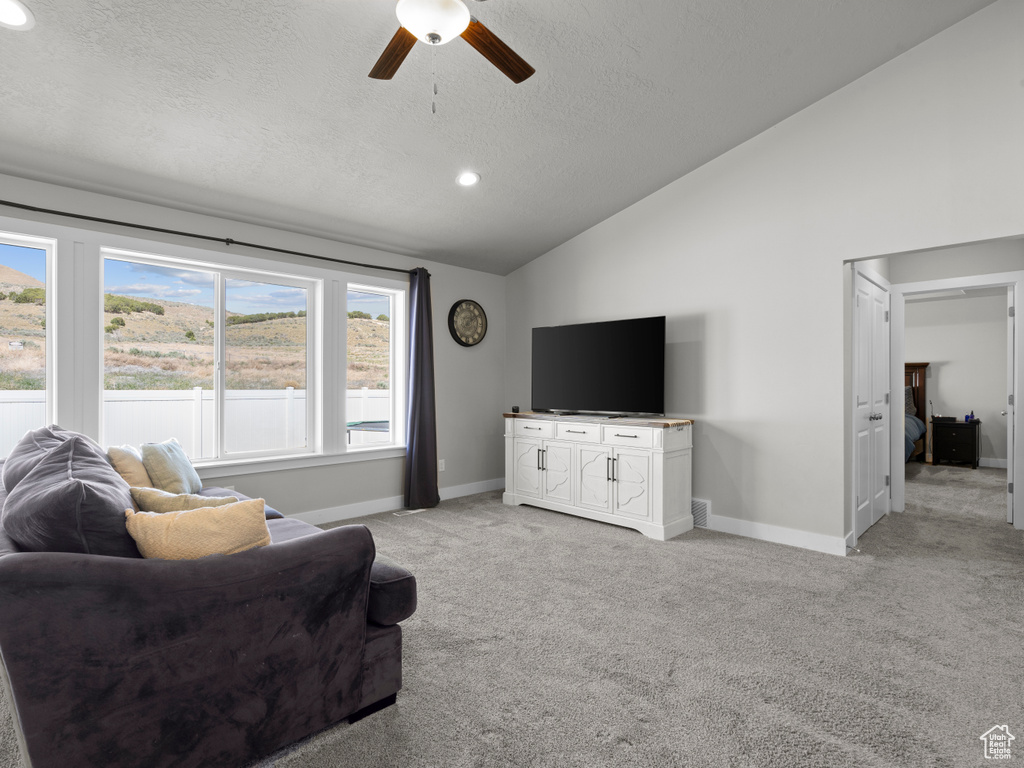 Living area with vaulted ceiling, ceiling fan, a textured ceiling, light colored carpet, and baseboards