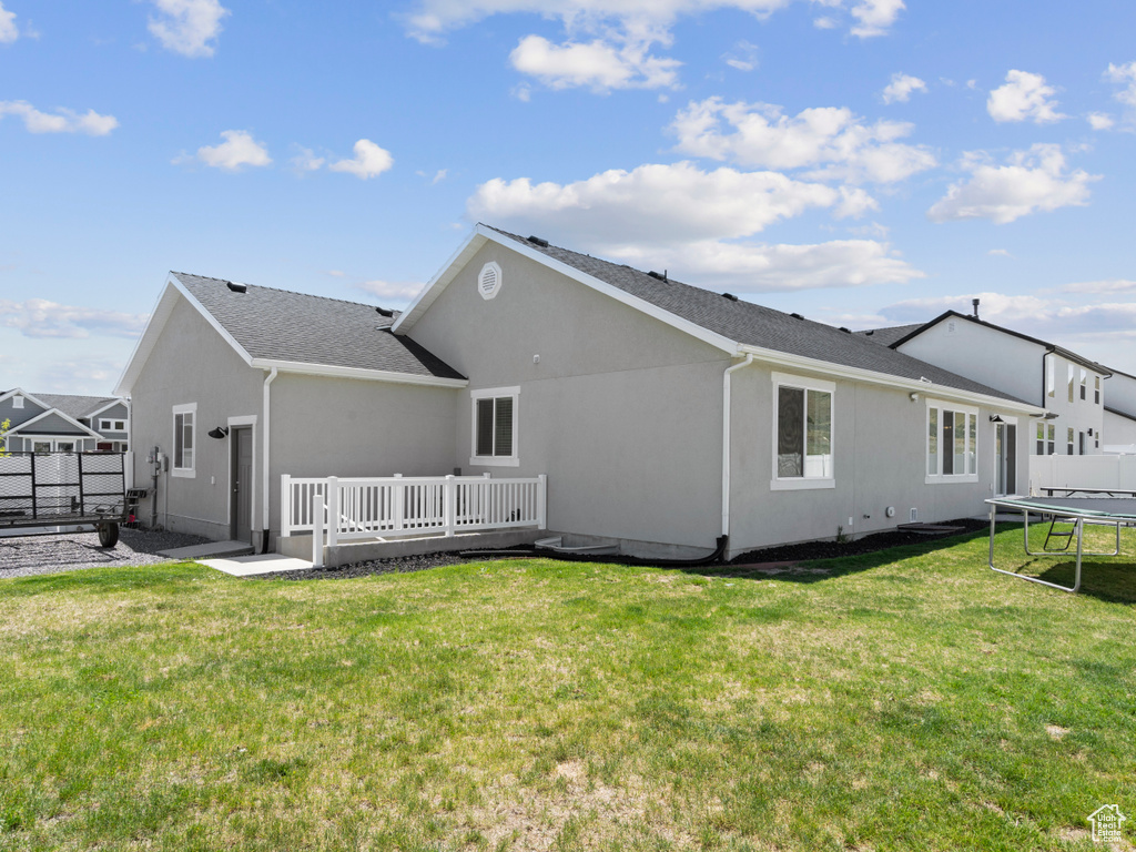 Rear view of house featuring a trampoline, a wooden deck, and stucco siding