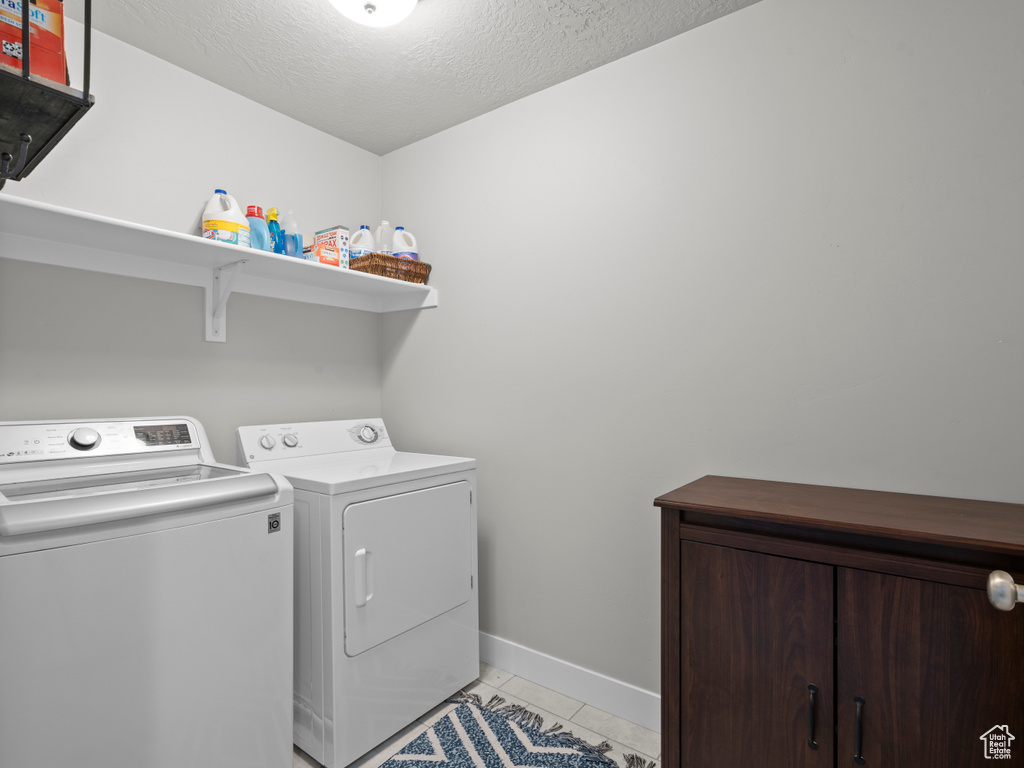 Clothes washing area featuring separate washer and dryer, light tile patterned flooring, a textured ceiling, and baseboards