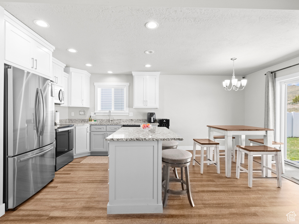 Kitchen featuring stainless steel appliances, light wood-type flooring, a breakfast bar, a chandelier, and recessed lighting
