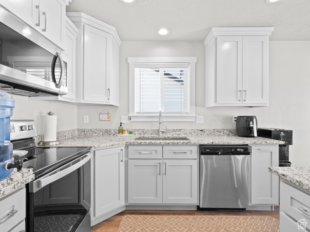 Kitchen with stainless steel appliances, a sink, recessed lighting, white cabinets, and light stone counters