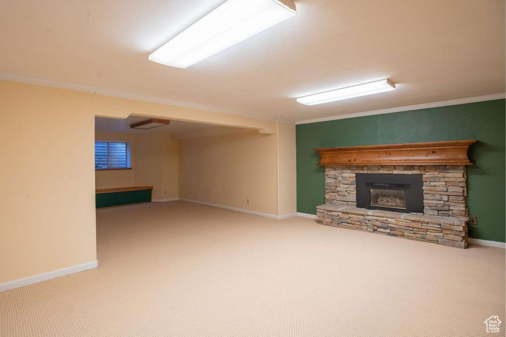 Unfurnished living room with crown molding, a stone fireplace, carpet flooring, and baseboards