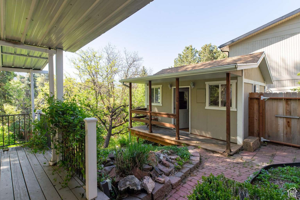 Property entrance with fence, a shingled roof, and a deck