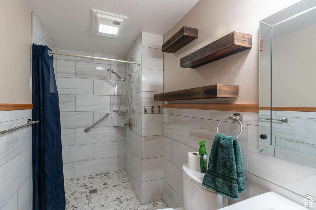Full bath featuring tiled shower, tile walls, toilet, and wainscoting