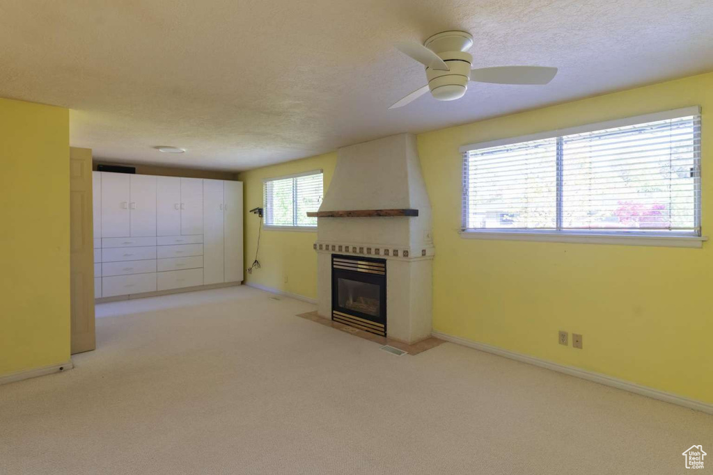 Unfurnished living room featuring a fireplace, light colored carpet, a ceiling fan, baseboards, and a textured ceiling