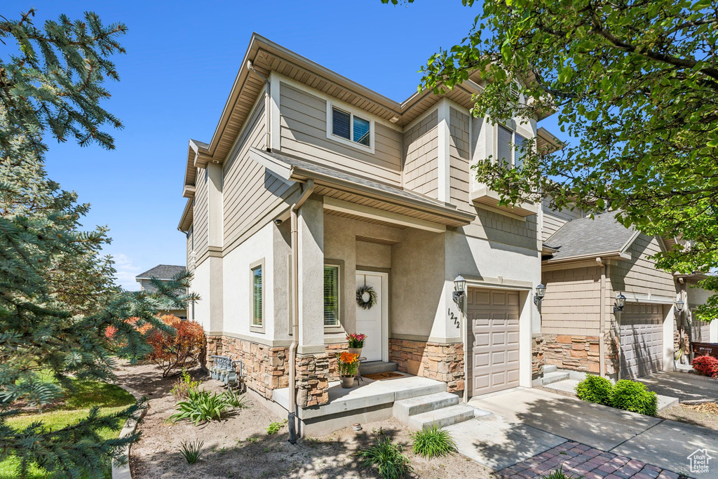 View of front facade with stone siding, a garage, driveway, and stucco siding