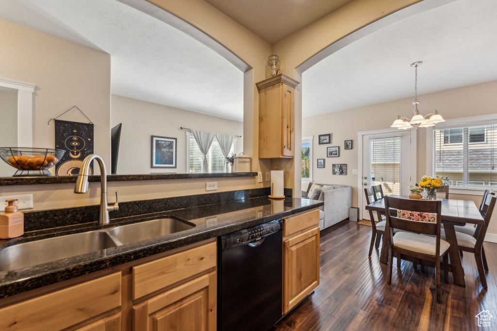 Kitchen featuring dishwasher, a sink, arched walkways, dark wood-type flooring, and dark stone counters