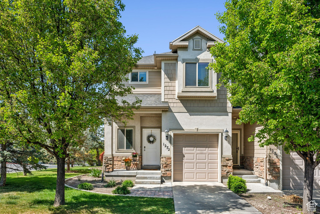 View of property featuring a garage, stone siding, driveway, and a front yard
